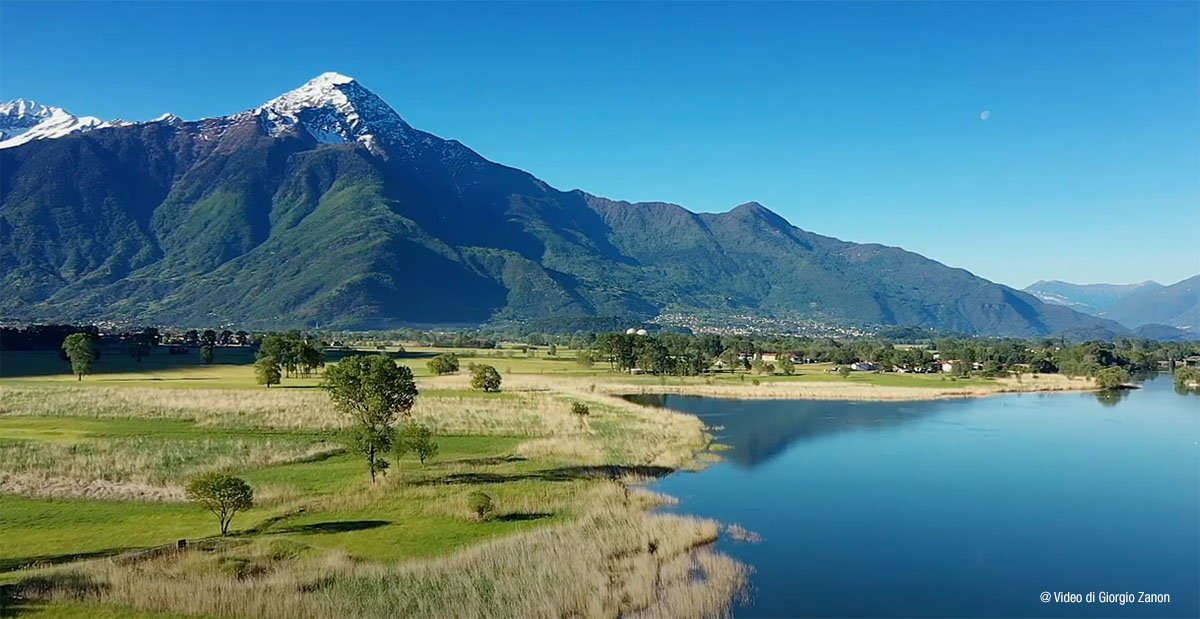 Riserva Naturale Pian di Spagna — pianura erbosa, fiume e monte innevato sullo sfondo